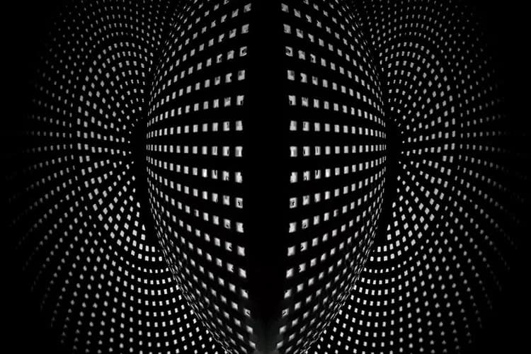 Black and white photograph of a modern building facade with illuminated windows creating geometric patterns that recede into perspective.