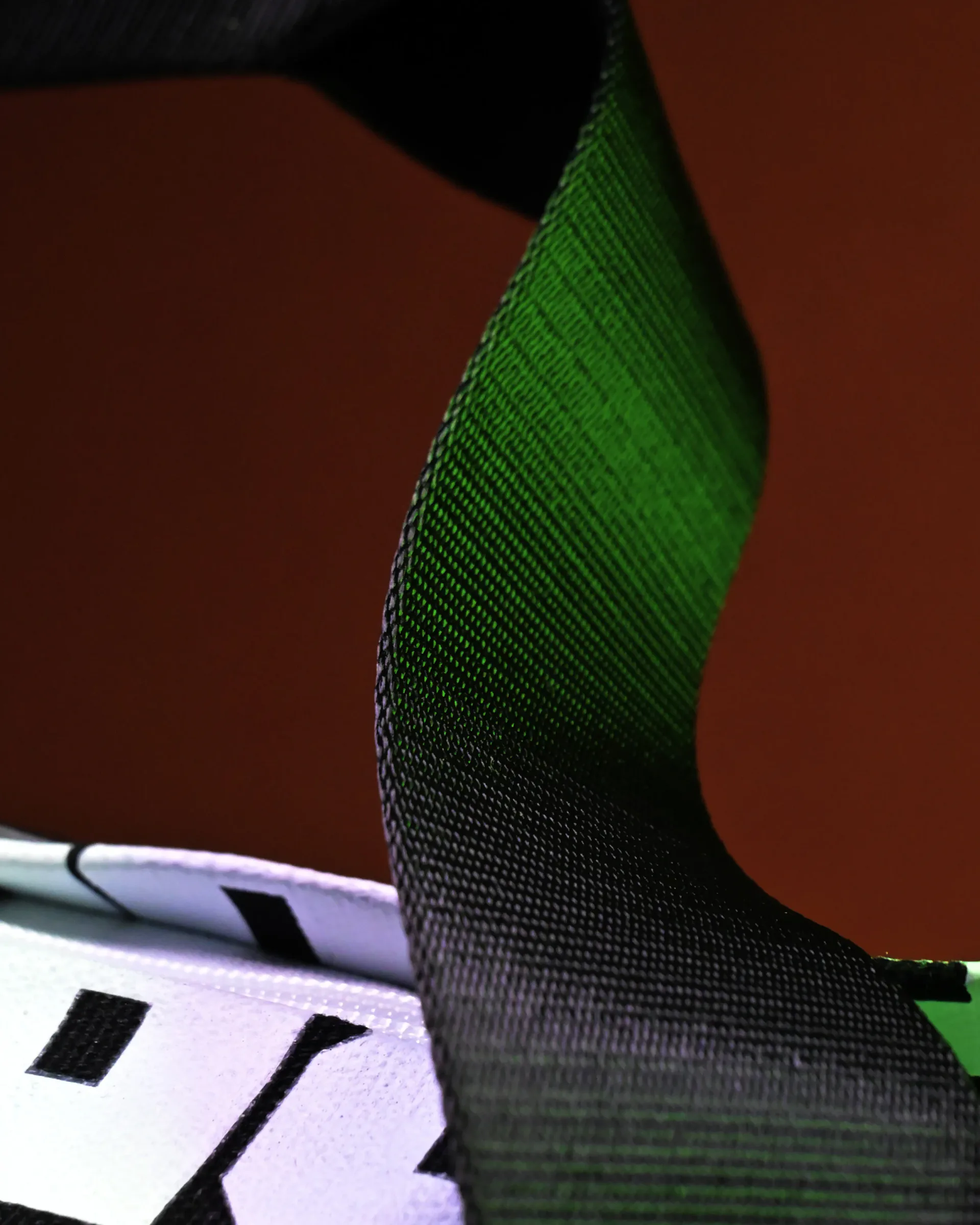 Close-up detail of black and green ribbed fabric material on a bag, shot against warm reddish background.