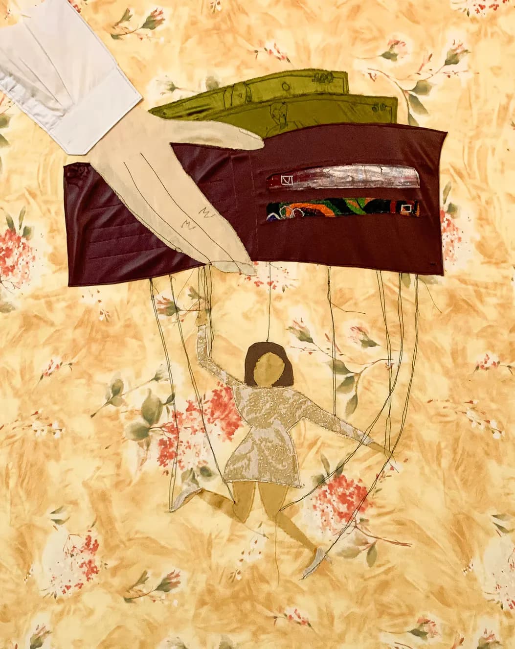 Fabric collage artwork of a figure puppet controlled by a wallet with currency, on floral background