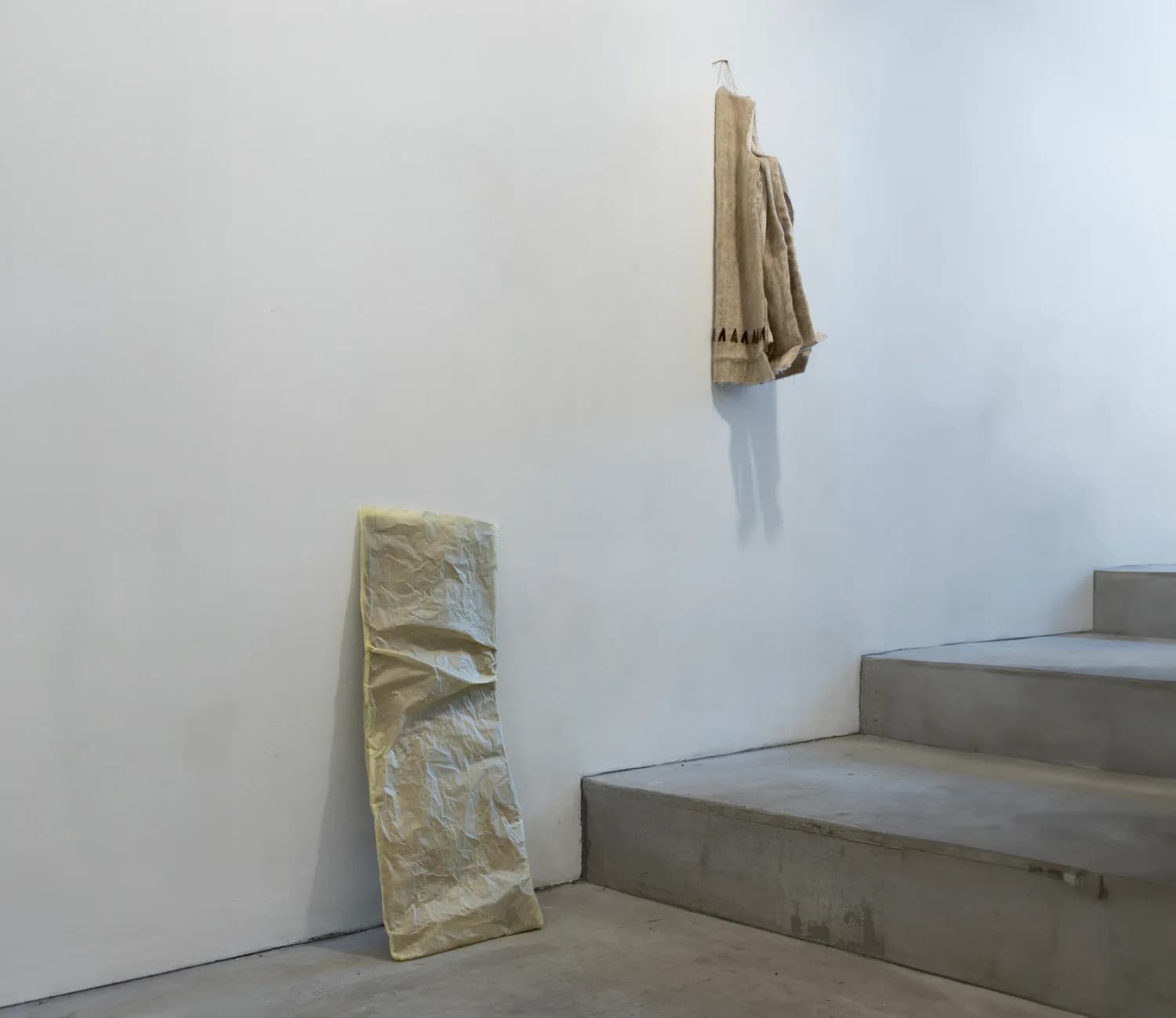 Gallery installation with suspended wax or resin textile hanging beside charcoal drawings on the wall