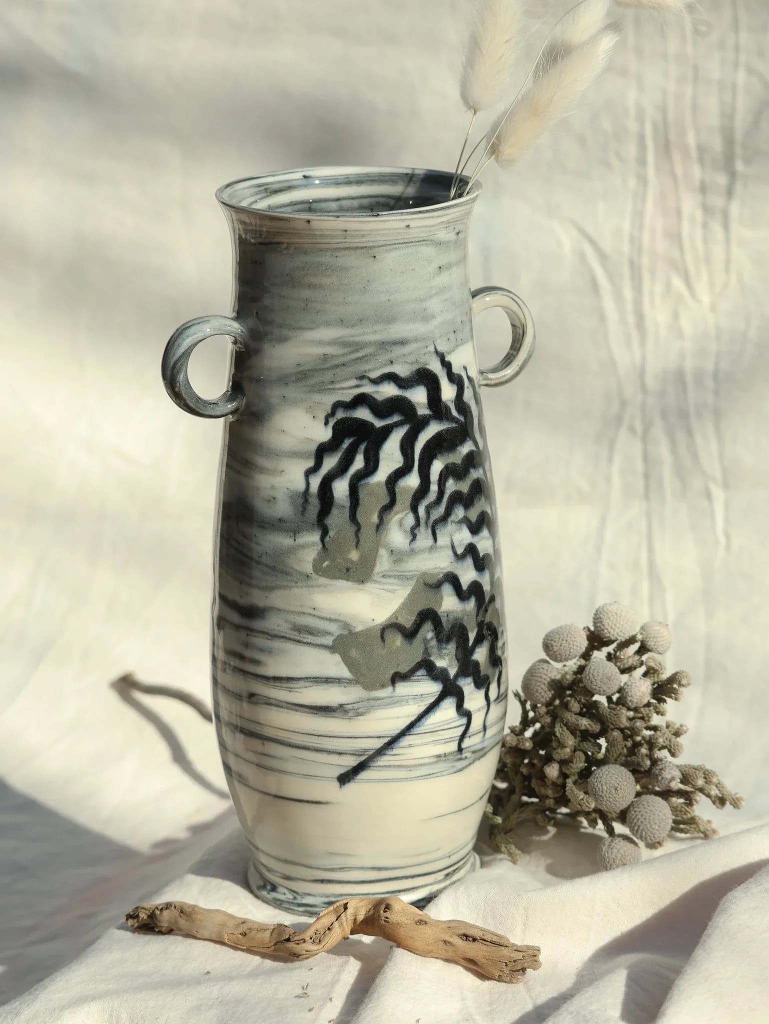 Tall cylindrical ceramic vessel by Alyssa Herrera with bold black wavy patterns on white-gray glaze, styled with natural objects.