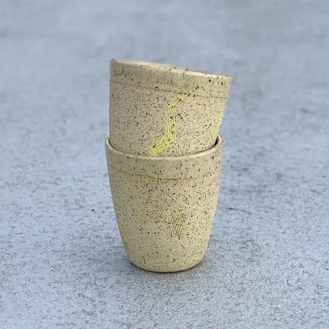 Stacked ceramic cups in speckled cream and yellow glaze with visible seam line, minimalist design.