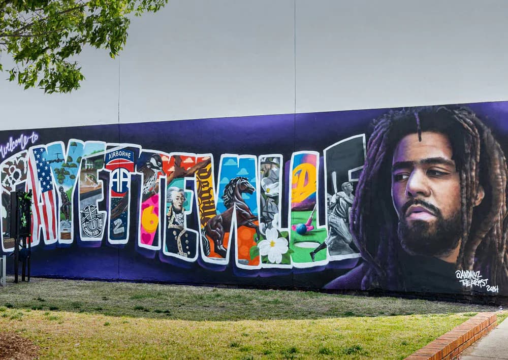 Large mural with purple background, colorful graffiti-style lettering, and portrait of bearded man with dreadlocks on right side.