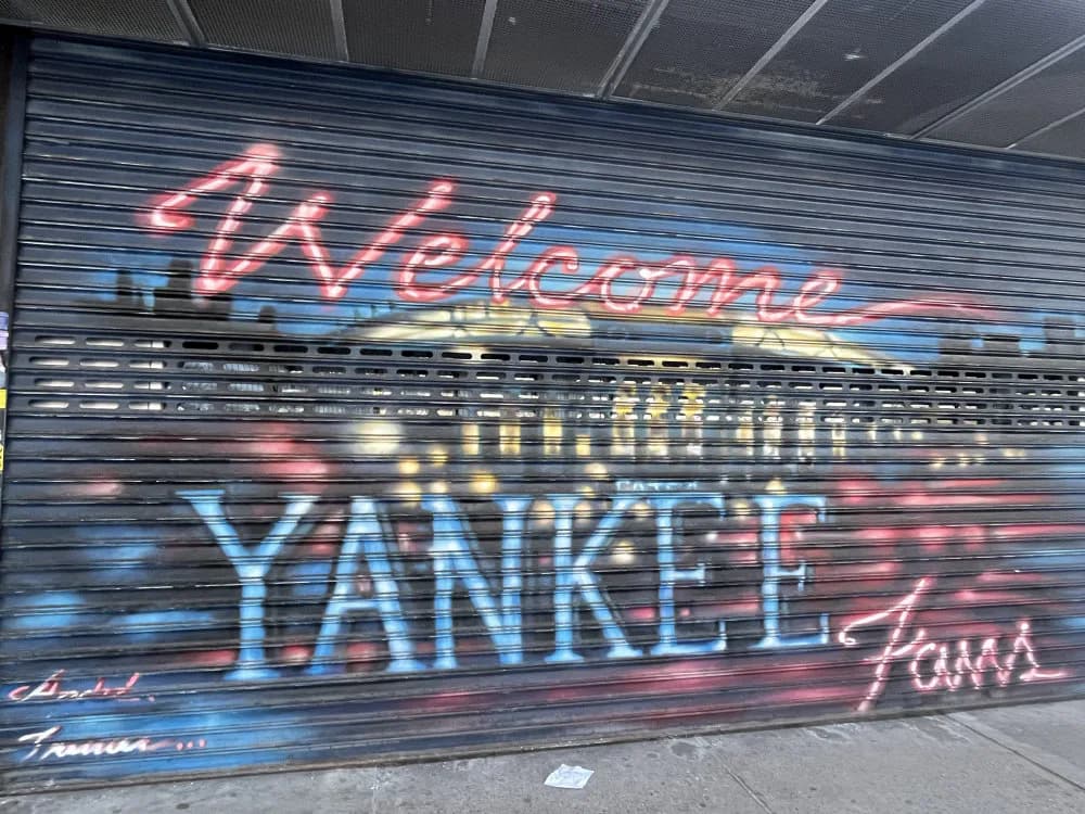Neon-style mural reading 'Welcome to the Bronx YANKEE Fans' in red and blue lettering on a metal shutter.
