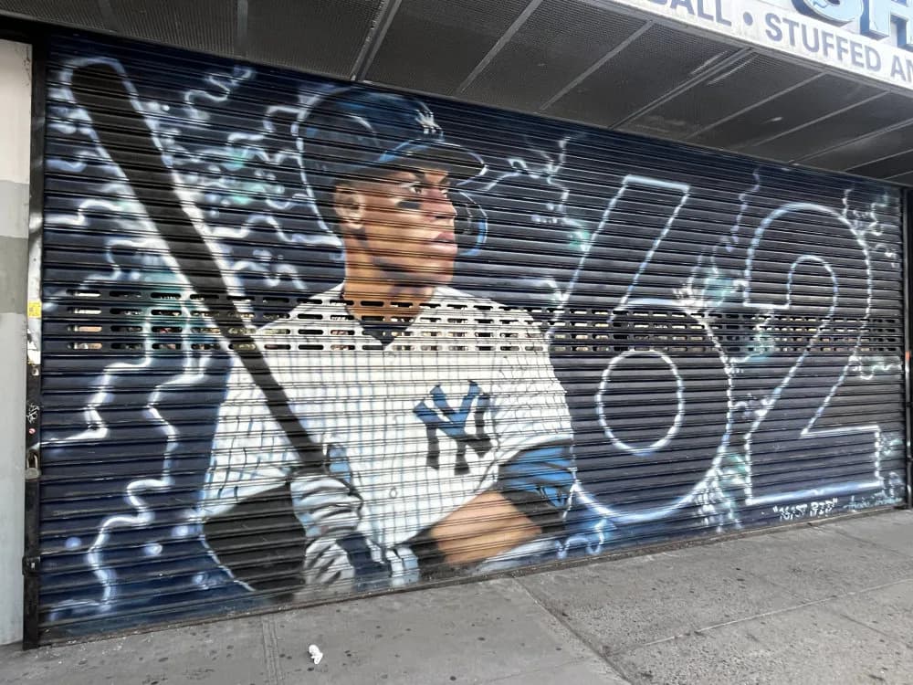 Mural of a Yankees player in white uniform holding a bat with electric blue accent effects on a metal security gate.