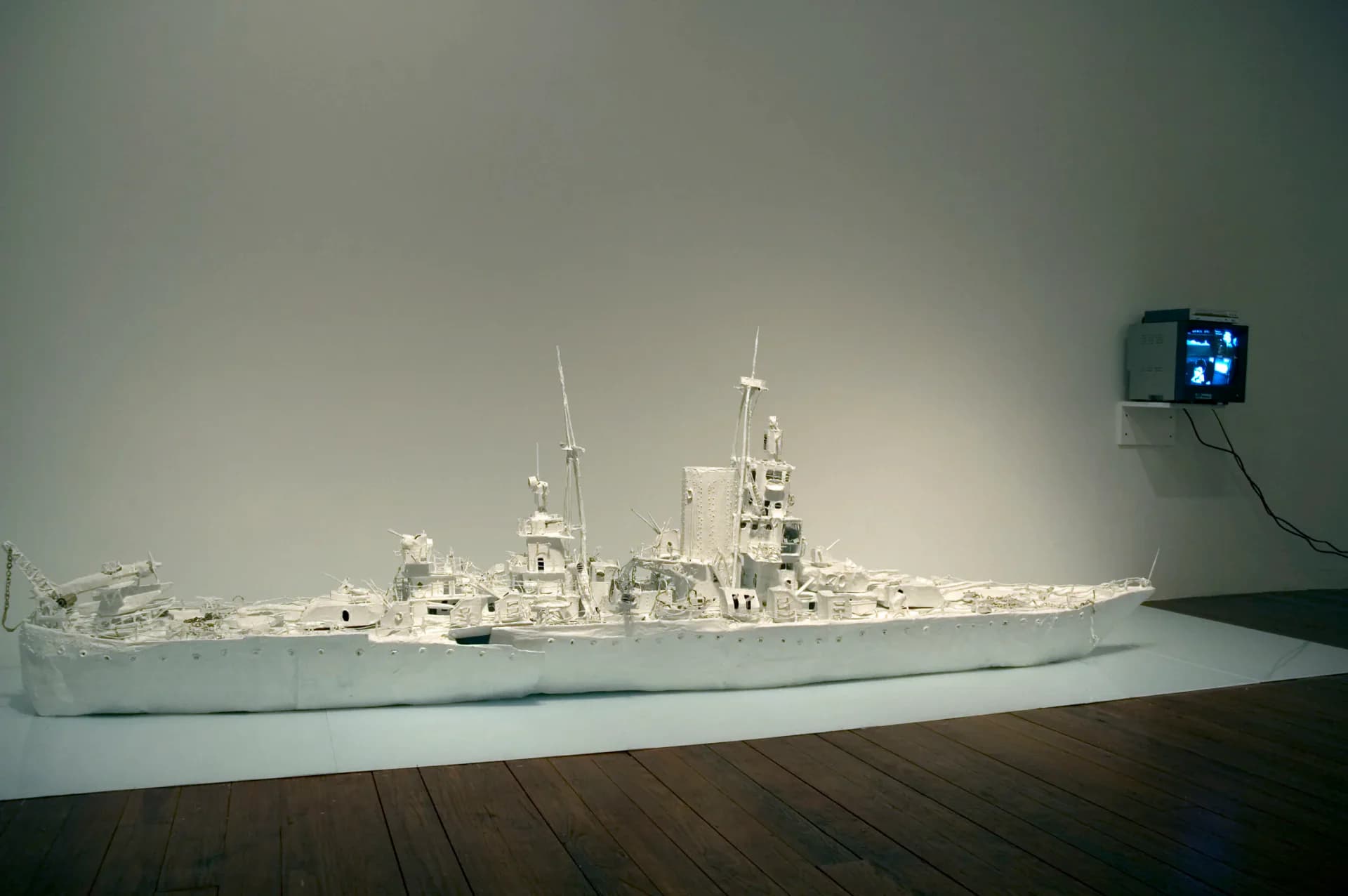 Large white battleship sculpture installed in gallery with video monitor