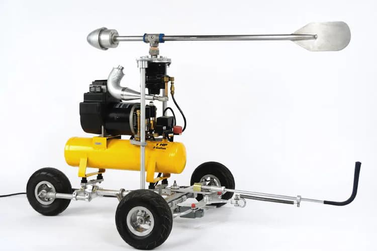 Mobile sculpture by Arnaldo Morales featuring a yellow pneumatic tank mounted on wheeled base with metal arm and counterweight extending horizontally.