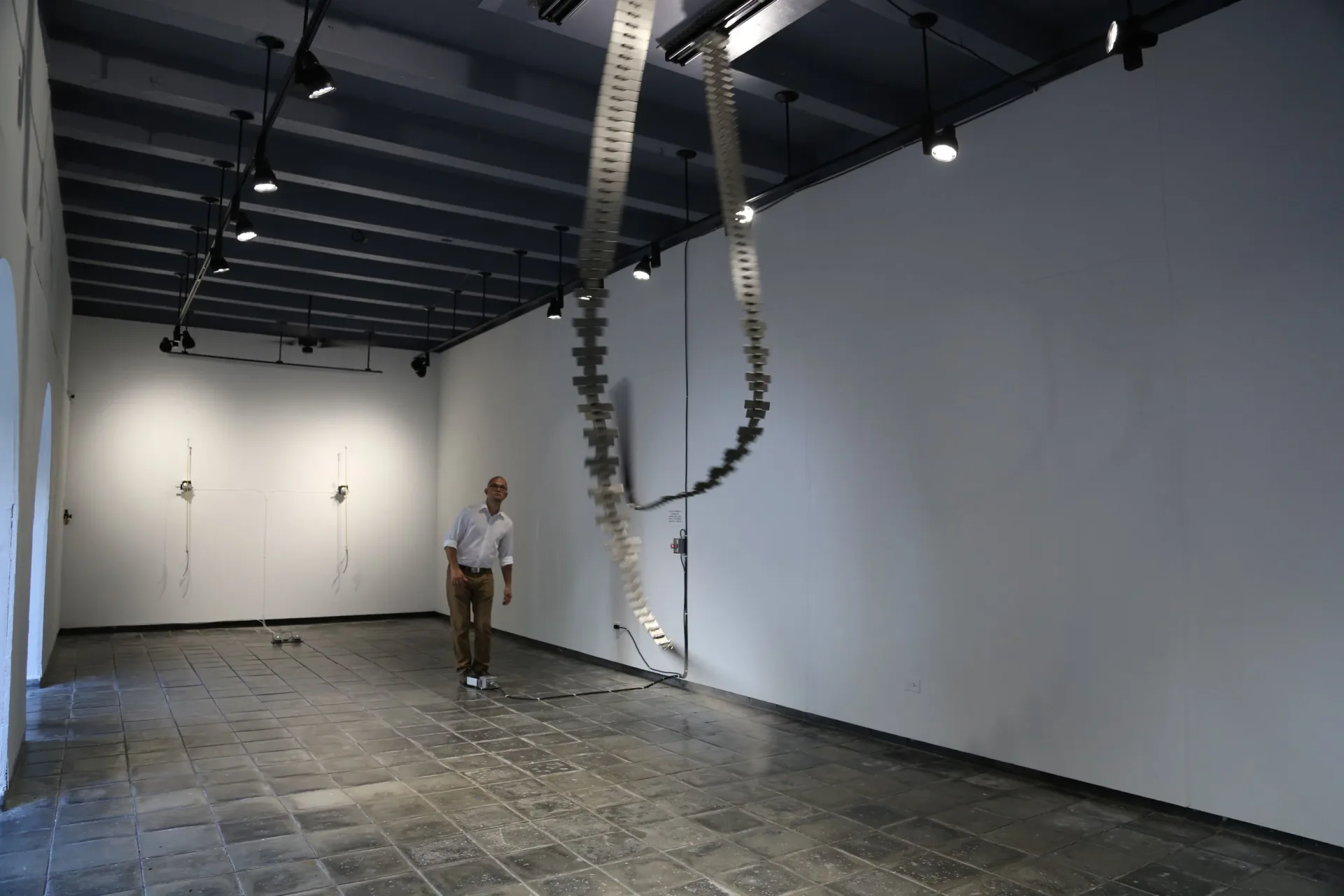 Industrial gallery interior with white walls, exposed ceiling infrastructure, and coiled hose installation running diagonally across space.