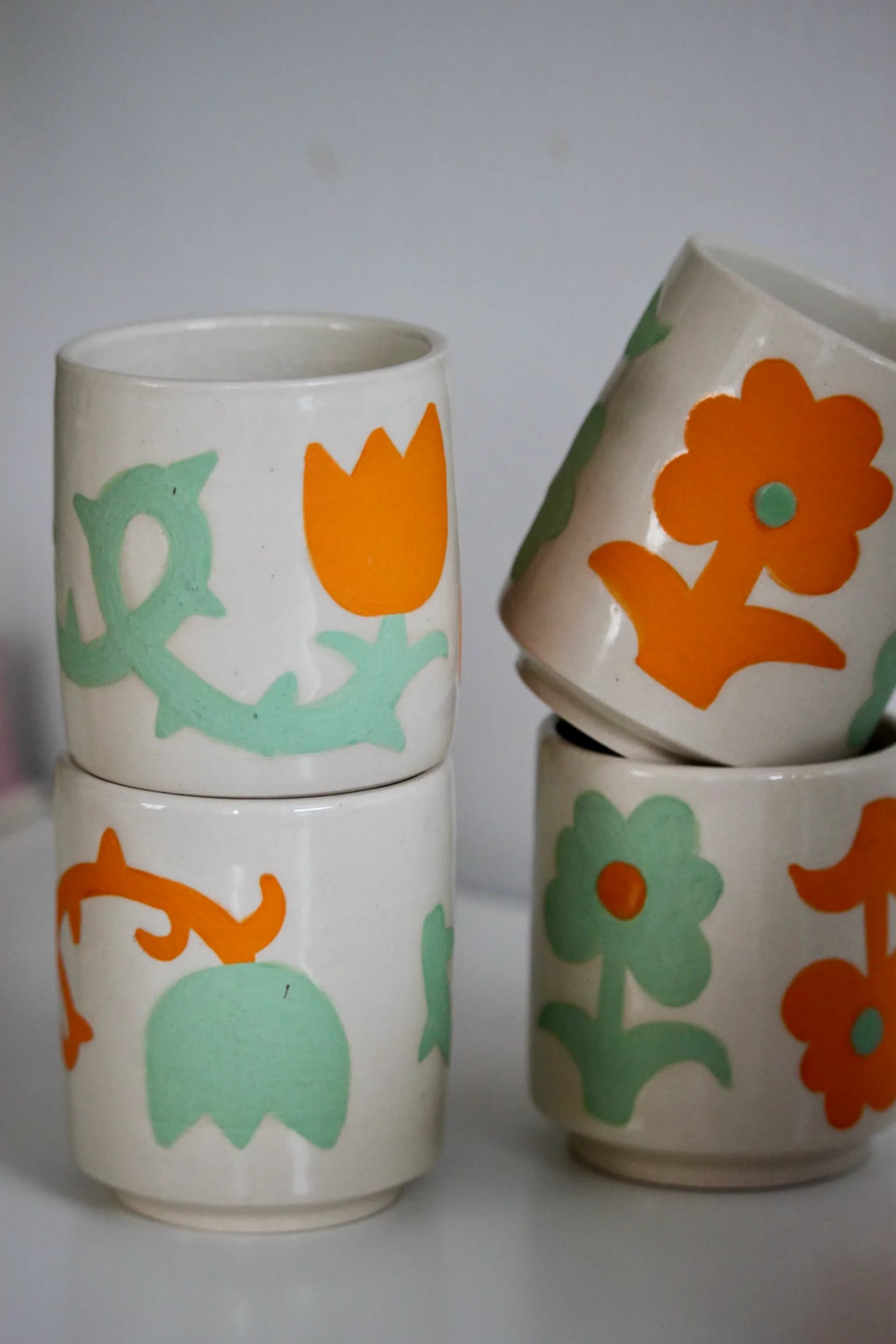 Group of four ceramic cups with orange and mint green botanical motifs stacked together