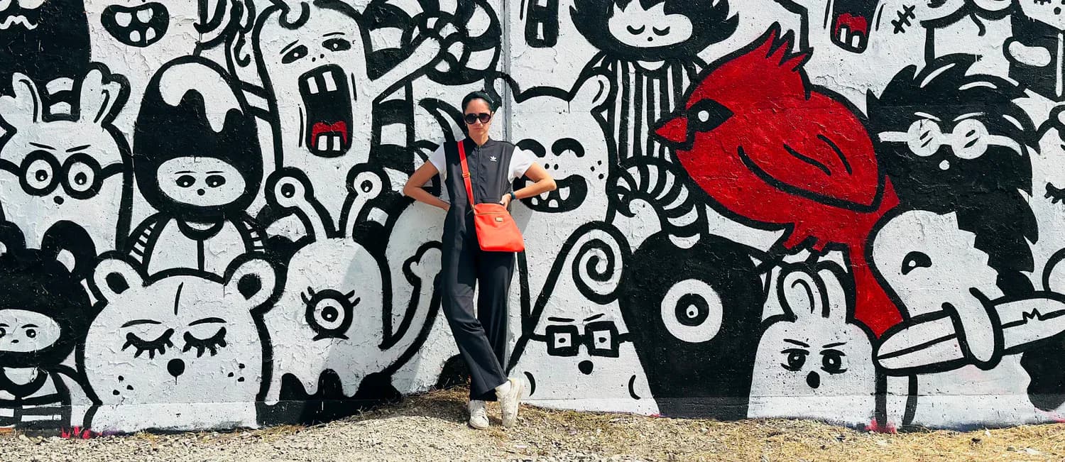 Person standing in front of black and white mural wall featuring intricate cartoon characters and a prominent red figure.