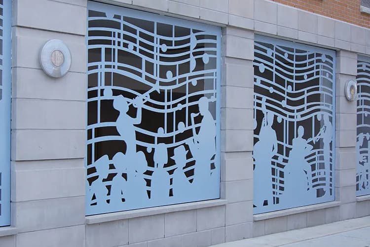 Light blue paper-cut panels mounted on a building facade depicting silhouetted dancers and musicians among musical notes and staves.