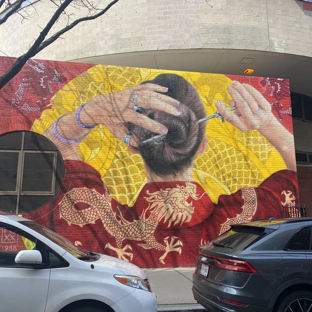 Mural featuring a person's hands against a bright yellow background with red dragon imagery, mixed-media style.
