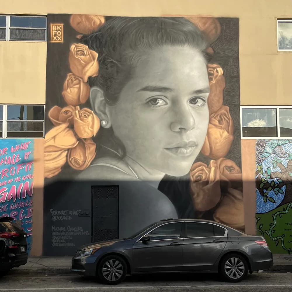Mural of a woman's face in grayscale with golden roses, rendered on a light building wall.