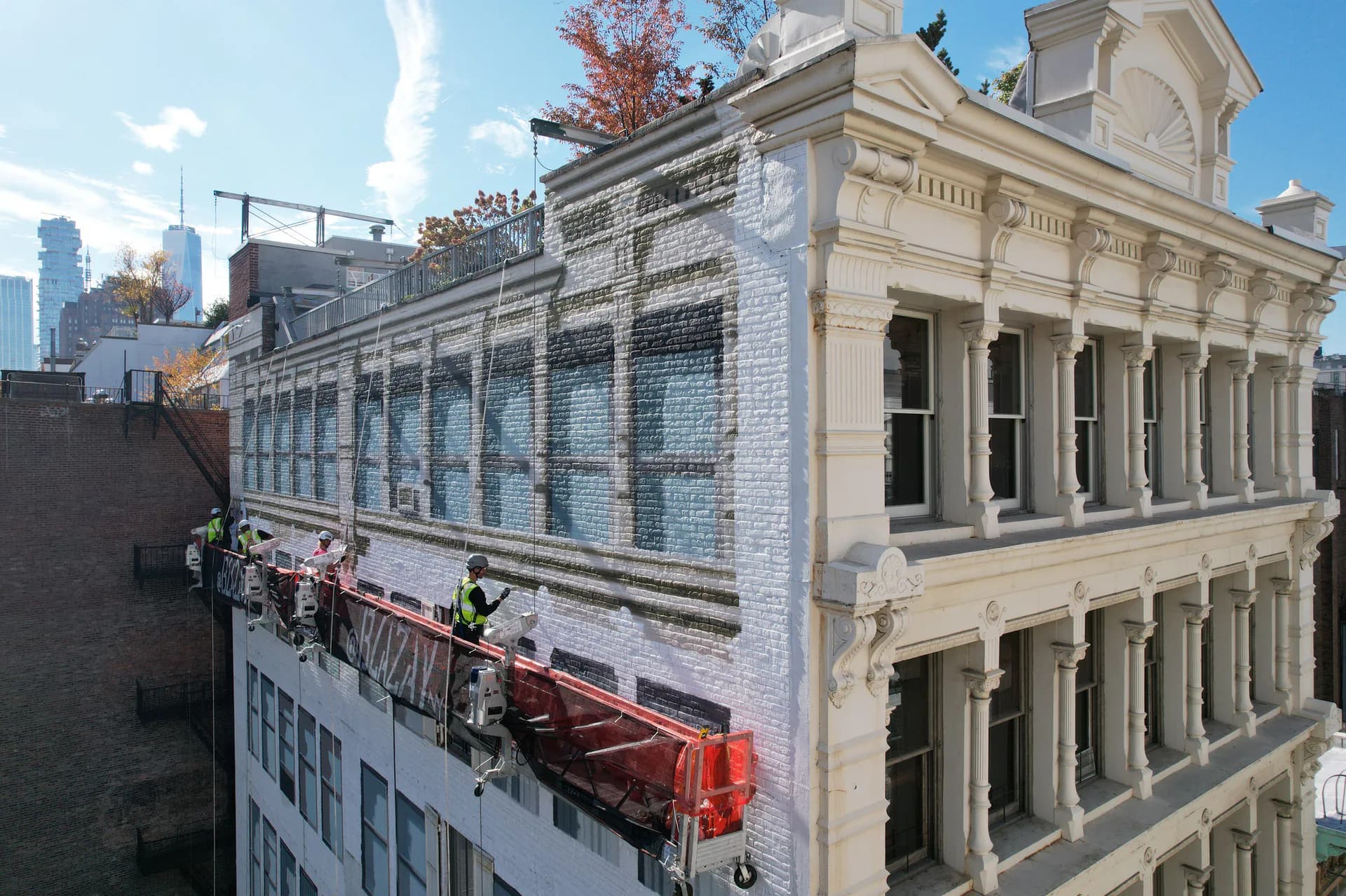 Photograph of a building exterior with white-painted brick facade, classical columns, and a large mural installation on adjacent structure.