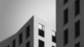 Blurred, low-contrast photograph of urban buildings in grayscale; subject indistinct.