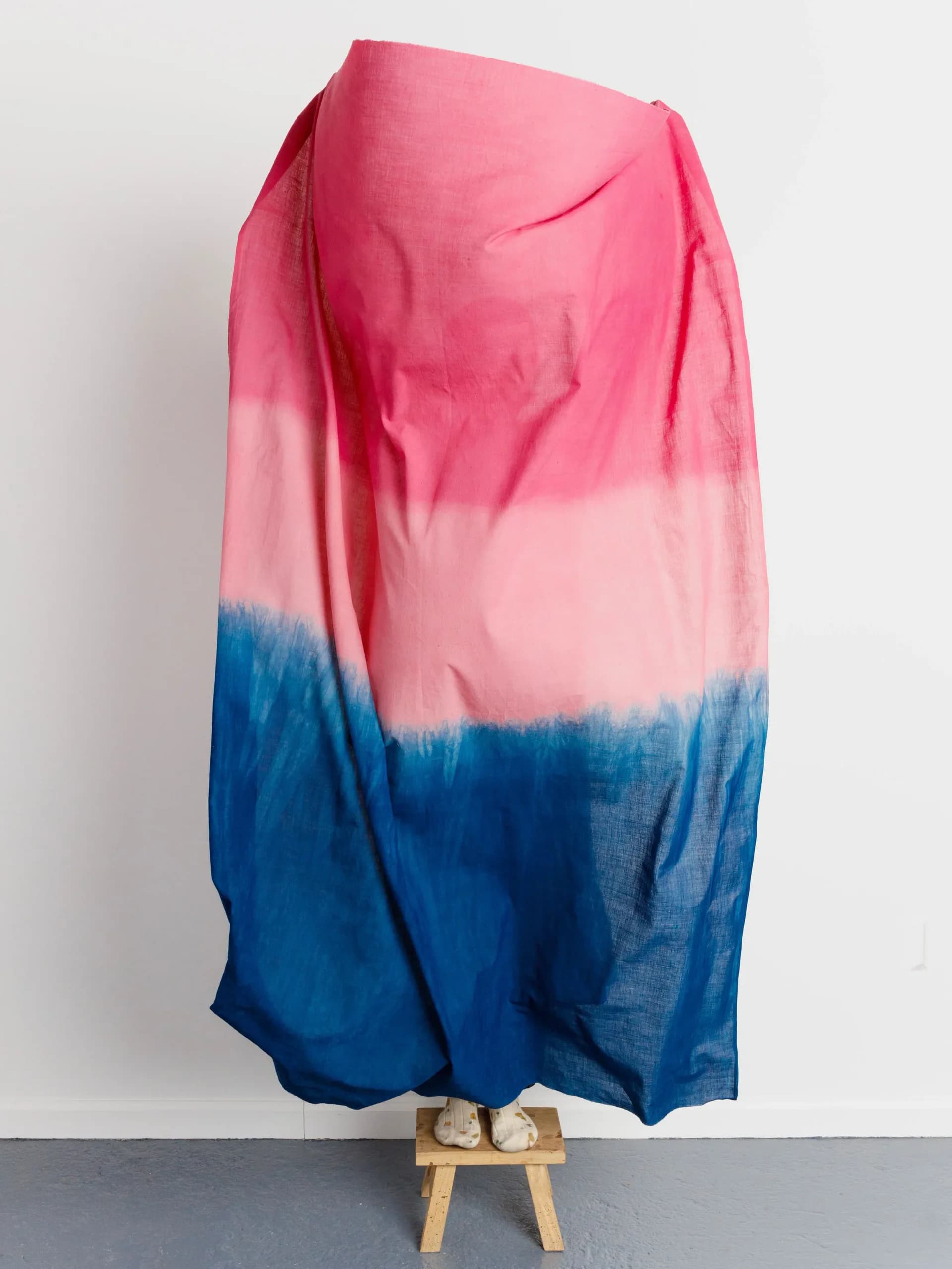 Large pink and blue dip-dyed linen textile draped over a stool against white wall