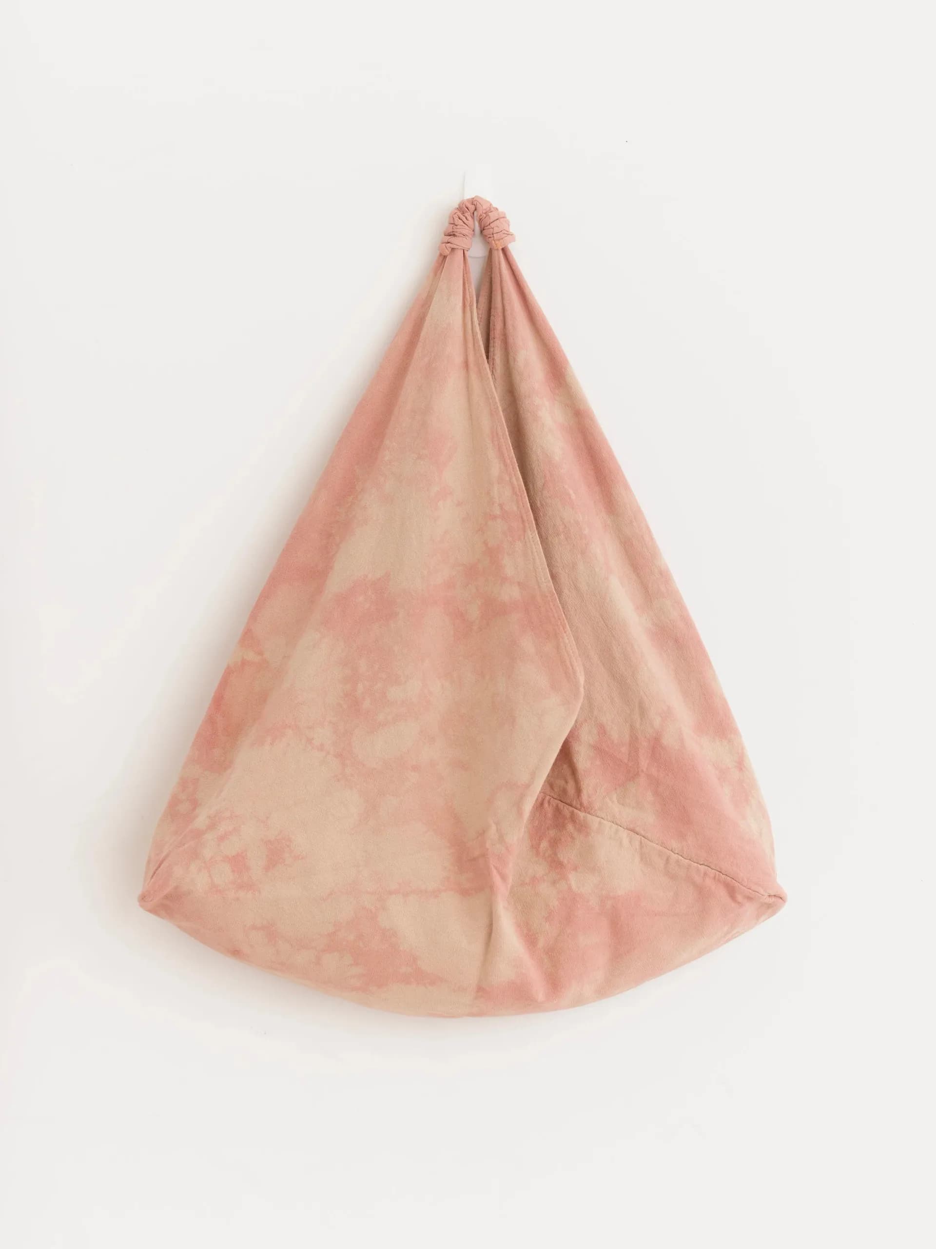 Soft pink shibori-dyed triangular fabric bag hung against white wall