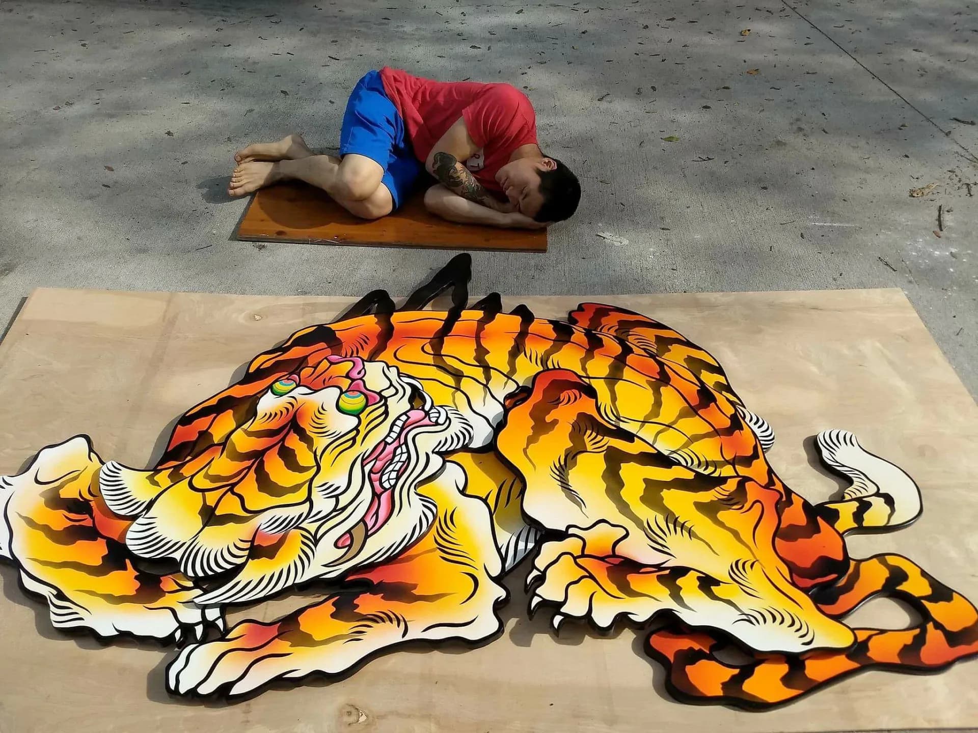 Large-scale paper mural of a tiger head with bold orange, black, and yellow stripes, installed in a public space with artist posing alongside.