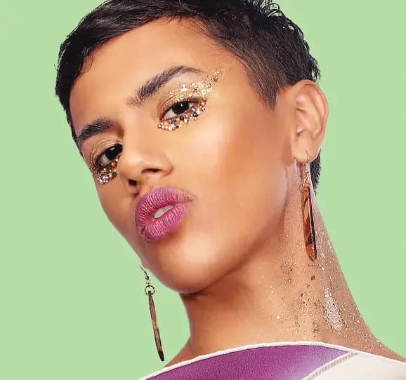 Model with gold glitter and jewel eye makeup on green background