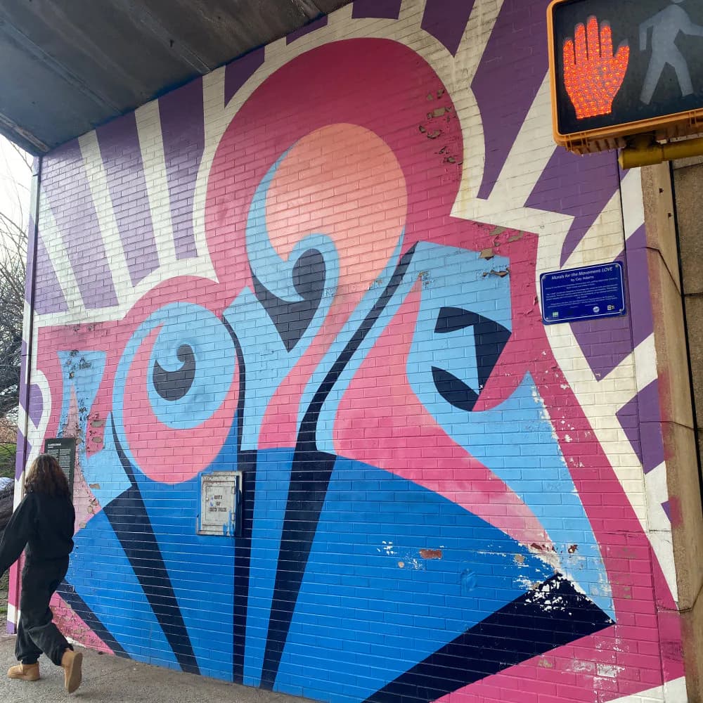 Colorful mural featuring abstract face with pink, blue, and cream geometric shapes and bold black outlines on brick wall.
