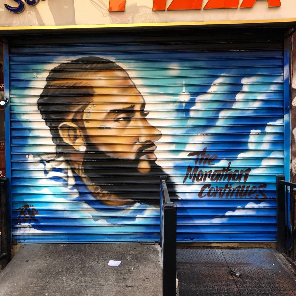 Mural portrait of a bearded man in profile painted on a blue corrugated metal shutter, with blue and white tones and text reading "The Morgantown Chronicles" by Charlie Doves.