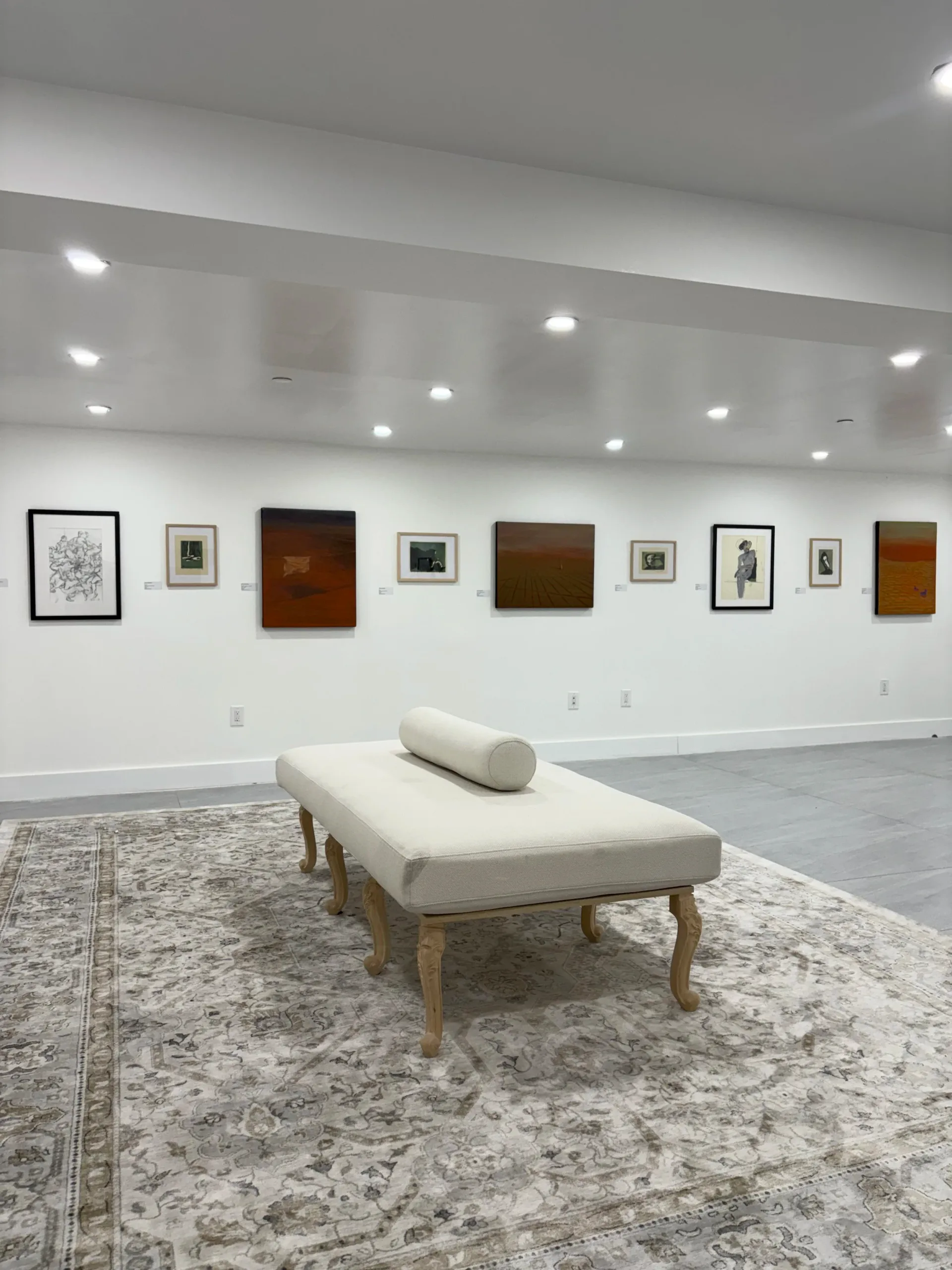 Gallery installation view with multiple framed artworks on white walls including paintings and drawings