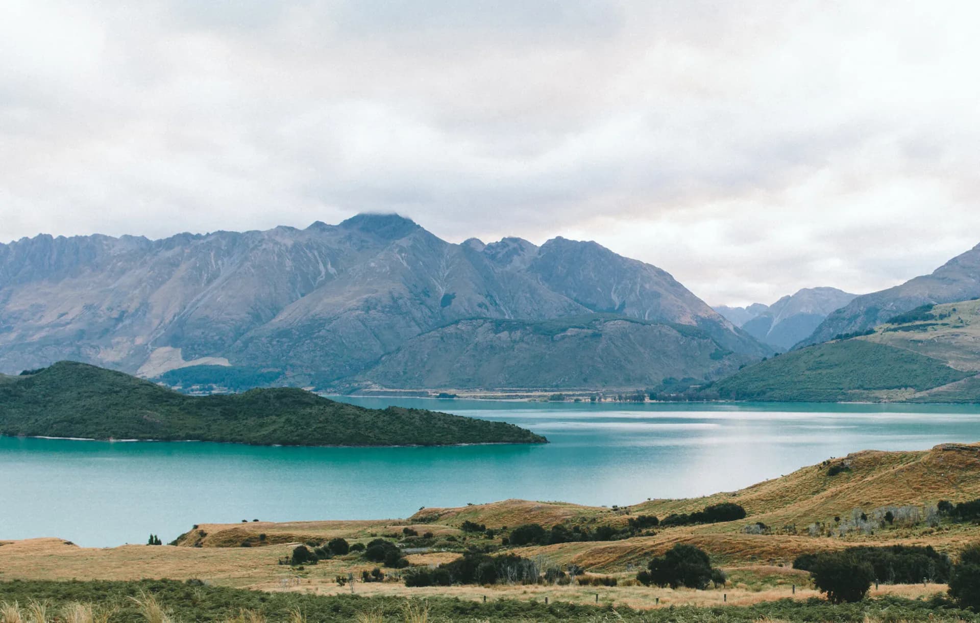 Wide landscape photograph of turquoise lake with rolling hills and mountain range, New Zealand