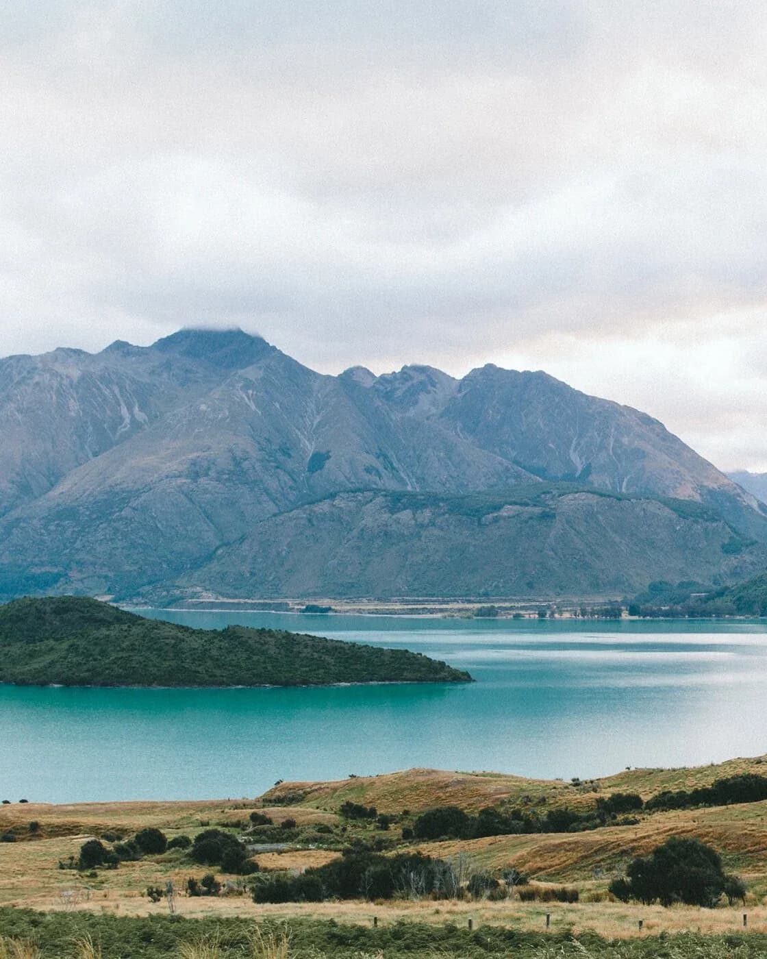 Timber cabin nestled in rolling alpine hills framed by pine branches, snow-capped peaks at dusk