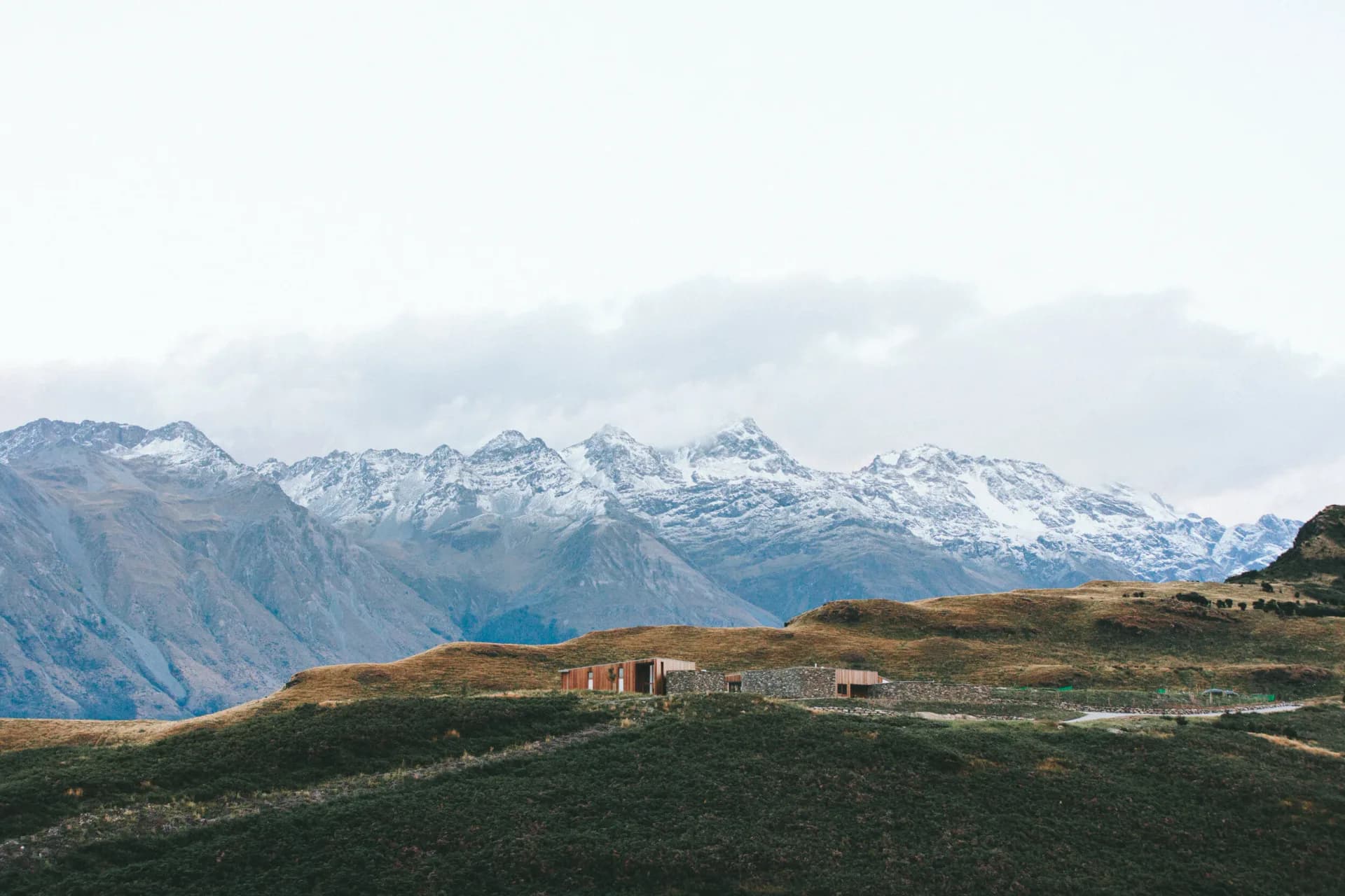 Modern timber building in wide alpine landscape with snow-covered mountains behind