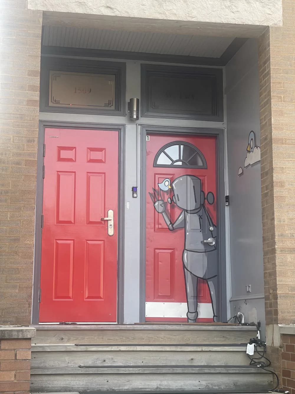 Stenciled mural on red doors of a brick building entrance showing a robot character with headphones and outstretched arms.