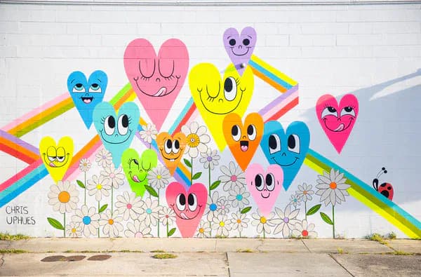 Completed colorful mural featuring smiling heart characters, rainbows, and flowers on a white wall by Chris Uphues
