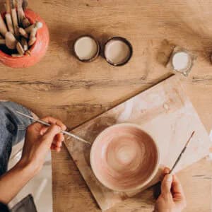 Hands painting glaze onto a ceramic bowl on a wooden surface