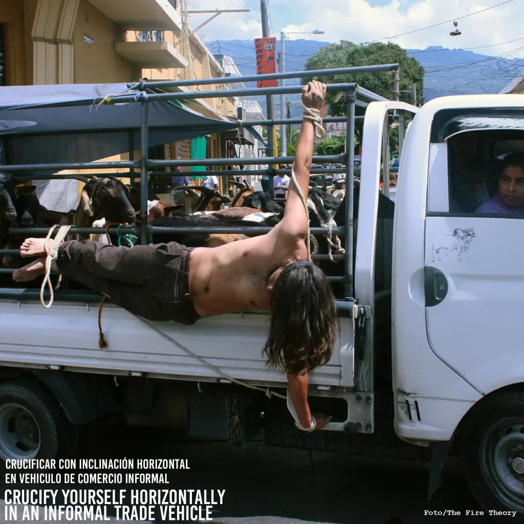 Performer crucified horizontally on side of livestock truck in urban street