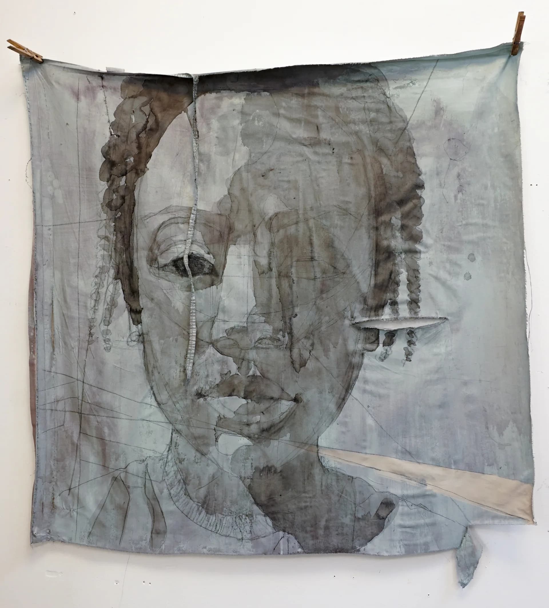 Large fabric portrait pinned to wall, face rendered in blue-grey ink washes with drips extending below onto the wall surface