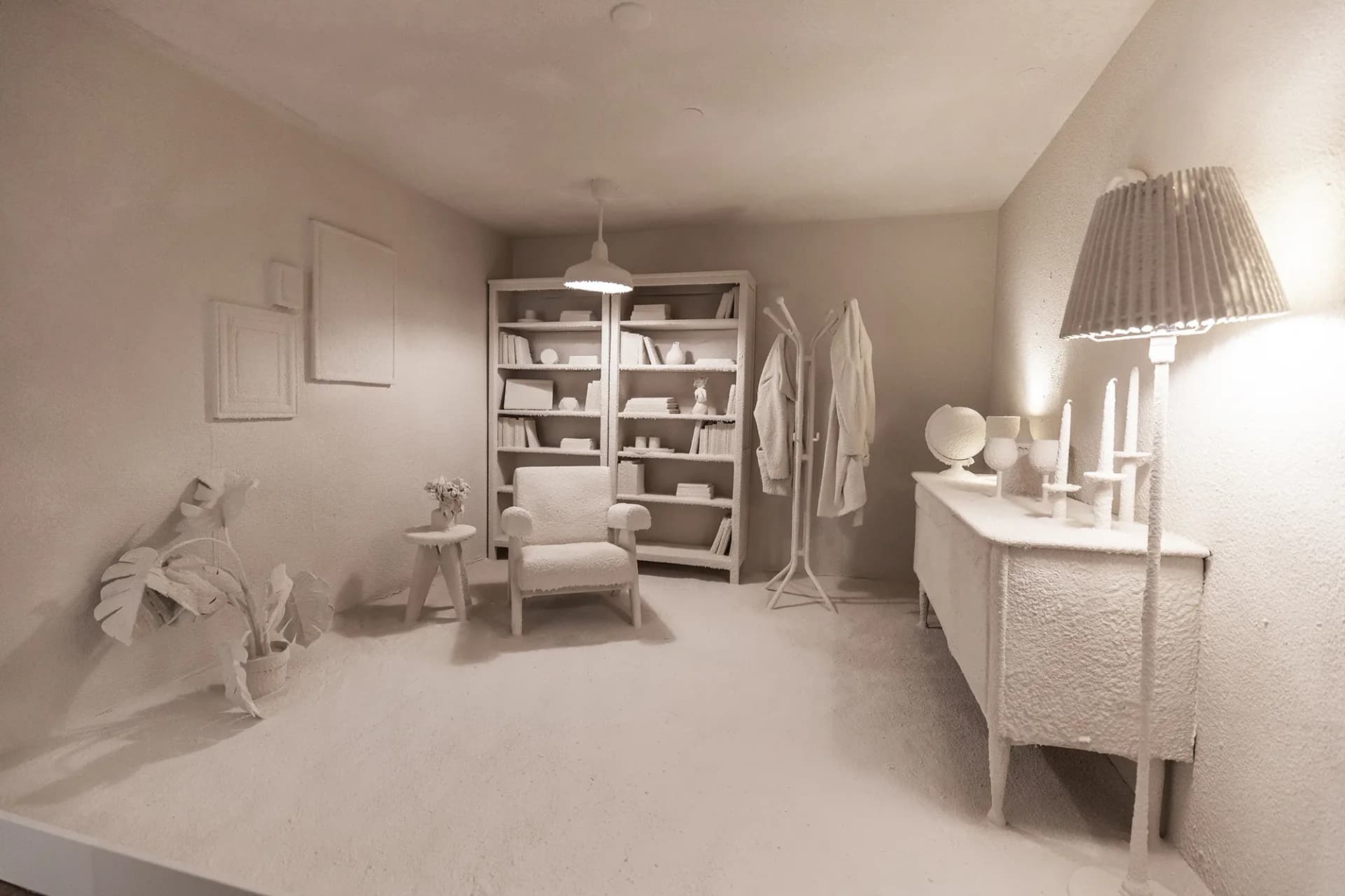 Monochromatic sculptural installation of an all-white minimalist bedroom interior with furniture, shelving, and décor rendered in plaster or similar material.
