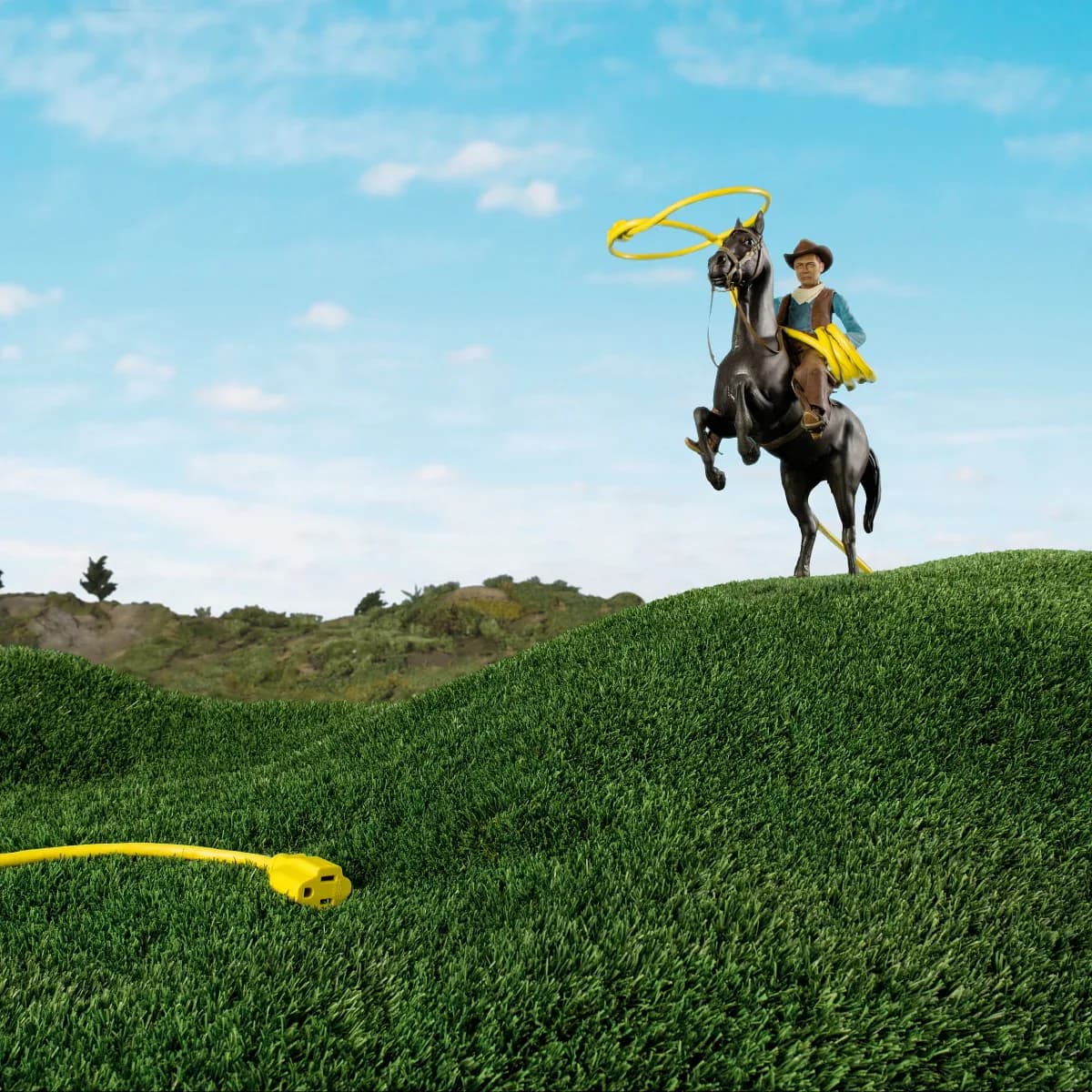 Miniature cowboy on horse lassoing a yellow extension cord across a grassy landscape