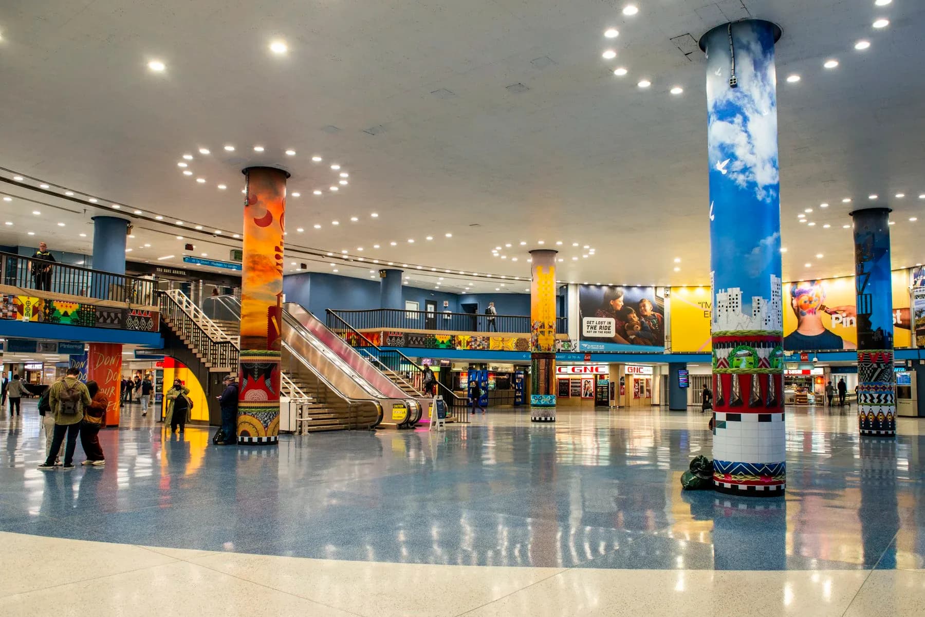 Modern airport or transit terminal interior with colorful painted support columns, bright lighting, and polished floor.