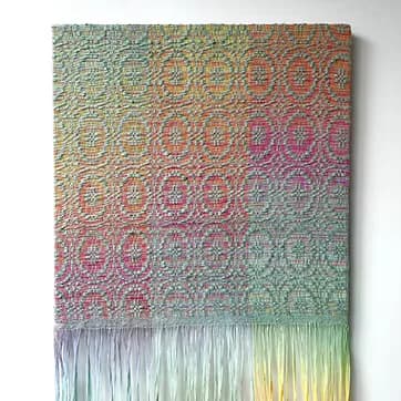 Colorful woven textile wall hanging with gradient rainbow pattern and fringe