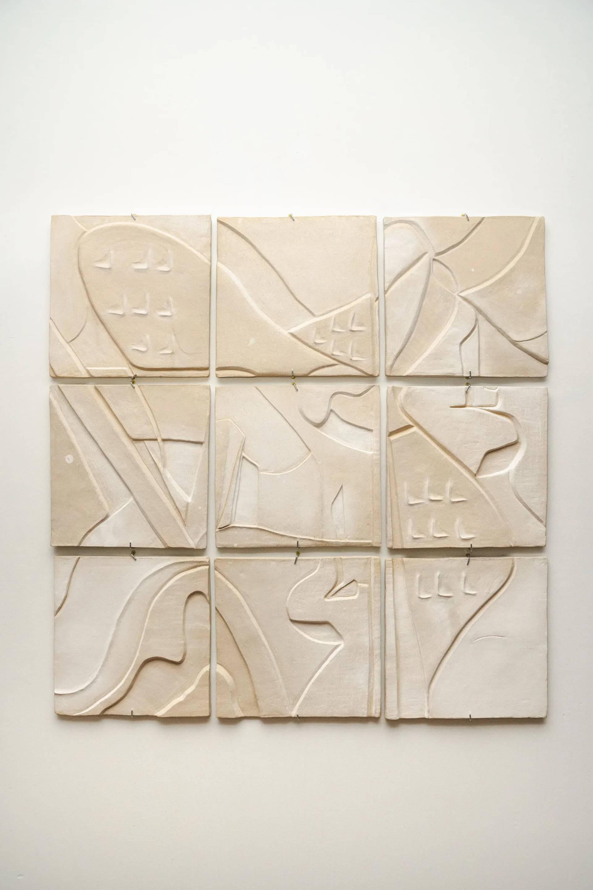 Nine ceramic relief tiles with carved abstract figures mounted on white wall