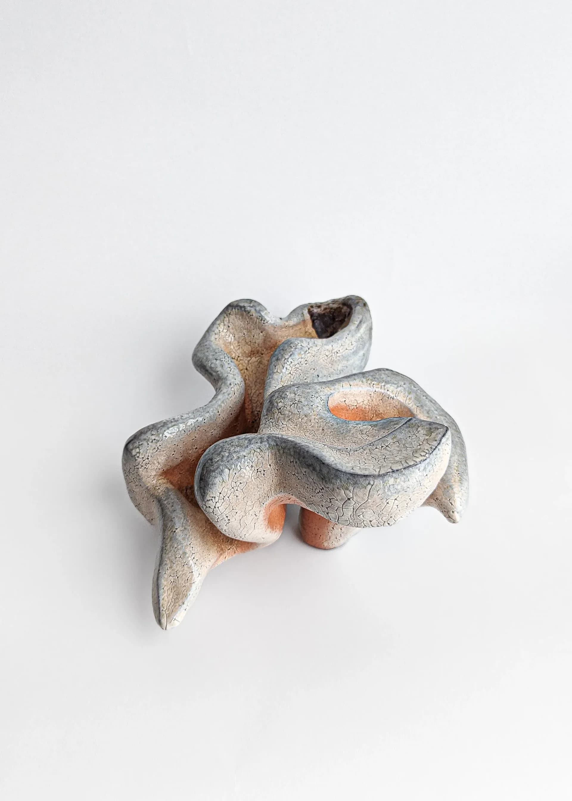 Matte white abstract ceramic sculpture with undulating organic form on neutral background