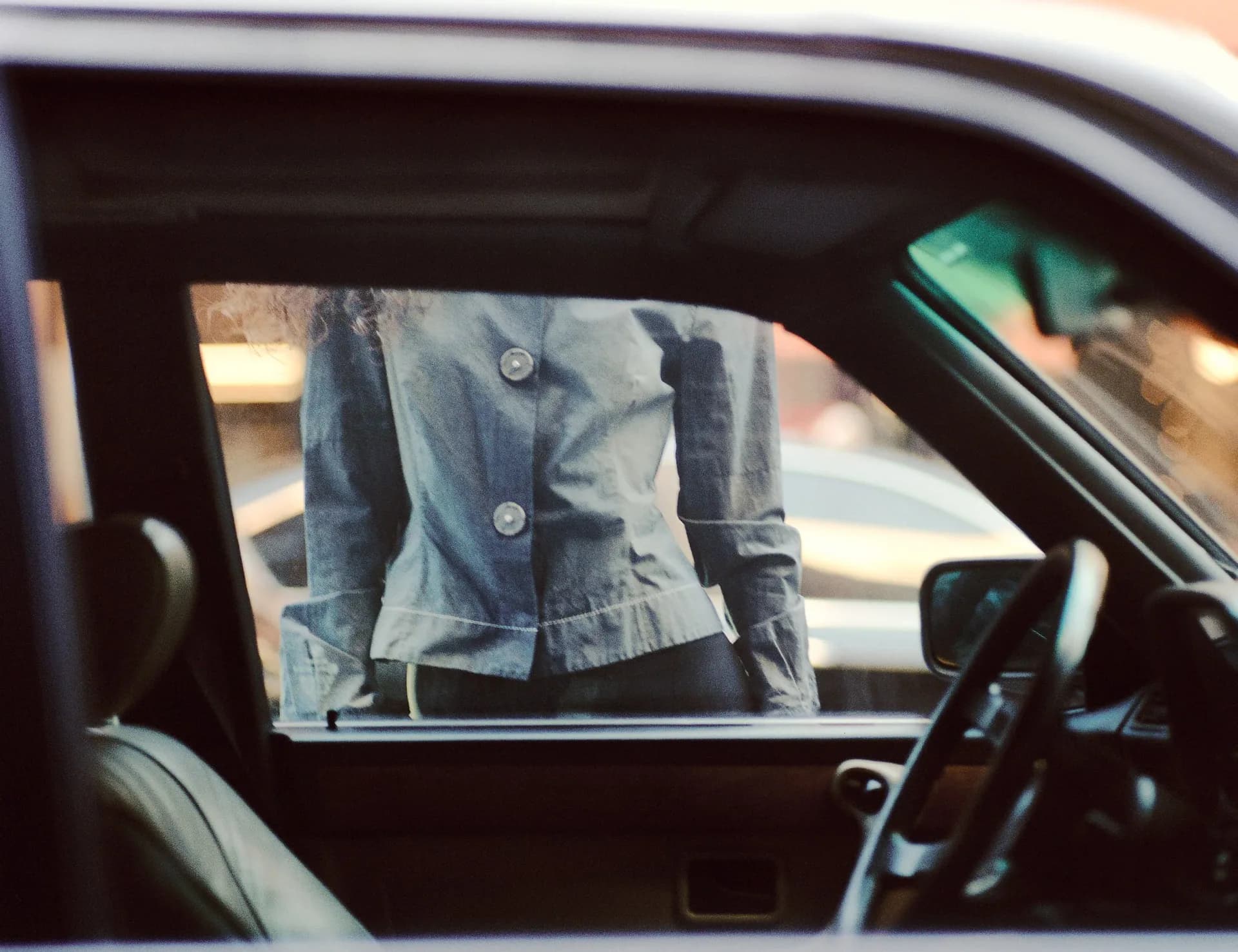 Woman's torso in blue jacket framed through a car window