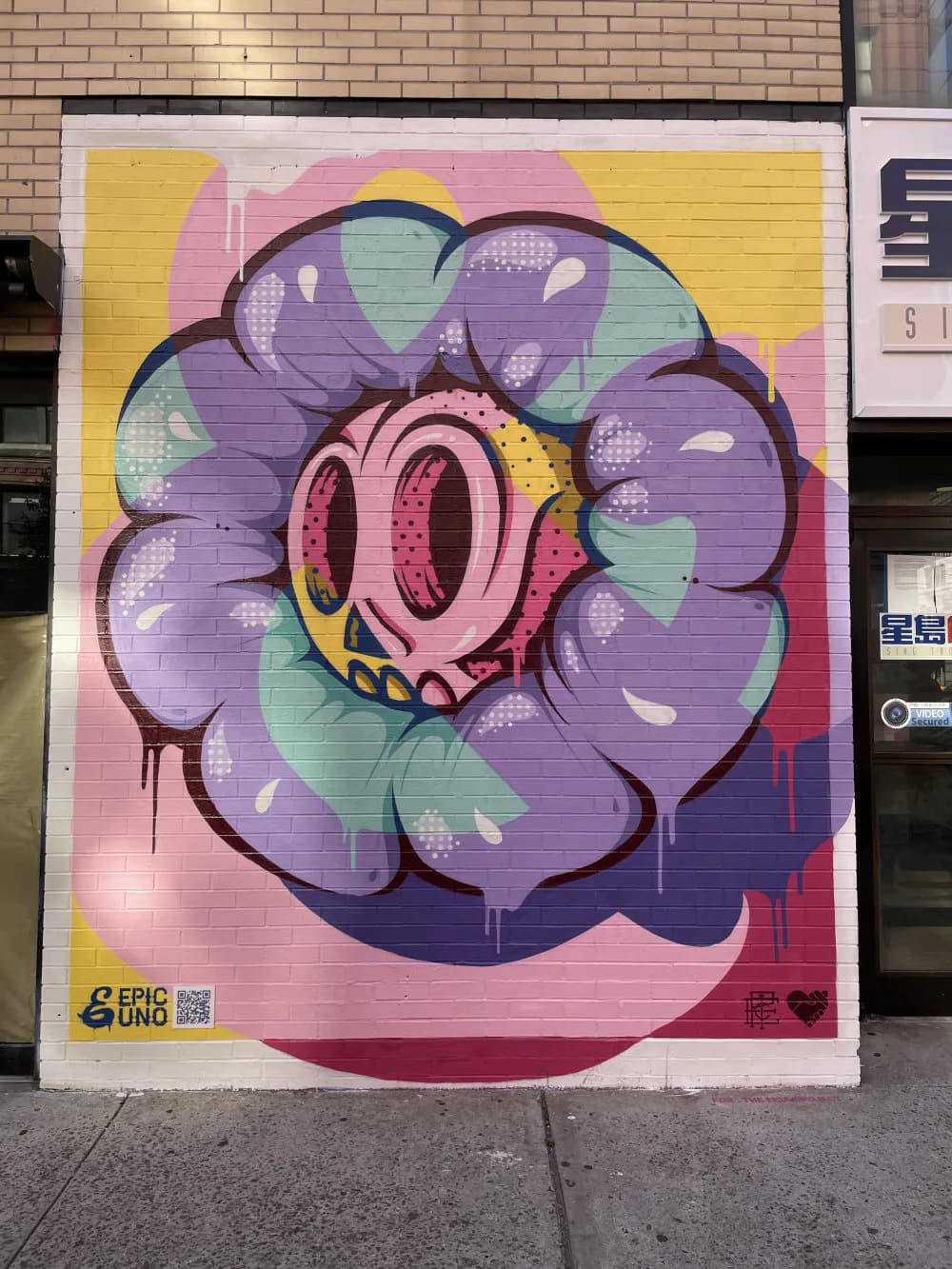 Colorful mural by Epic Uno featuring a large purple flower with pink center and bold black outline on yellow and pink background.