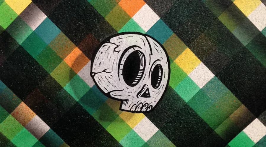 White hand-drawn skull character with large oval eyes centered on green and yellow diamond plaid pattern background.