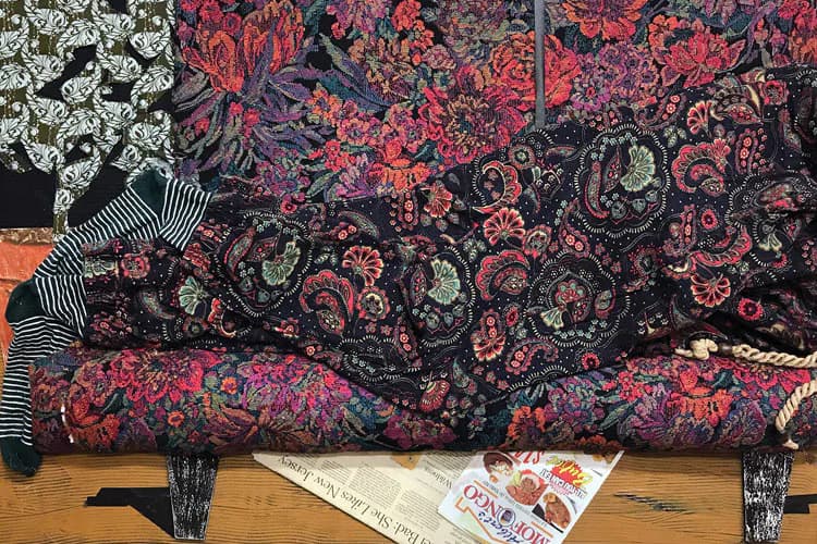 Ornate upholstered sofa with deep red and black damask-patterned fabric, wooden legs, displayed in an interior setting with newspapers and striped textile nearby.