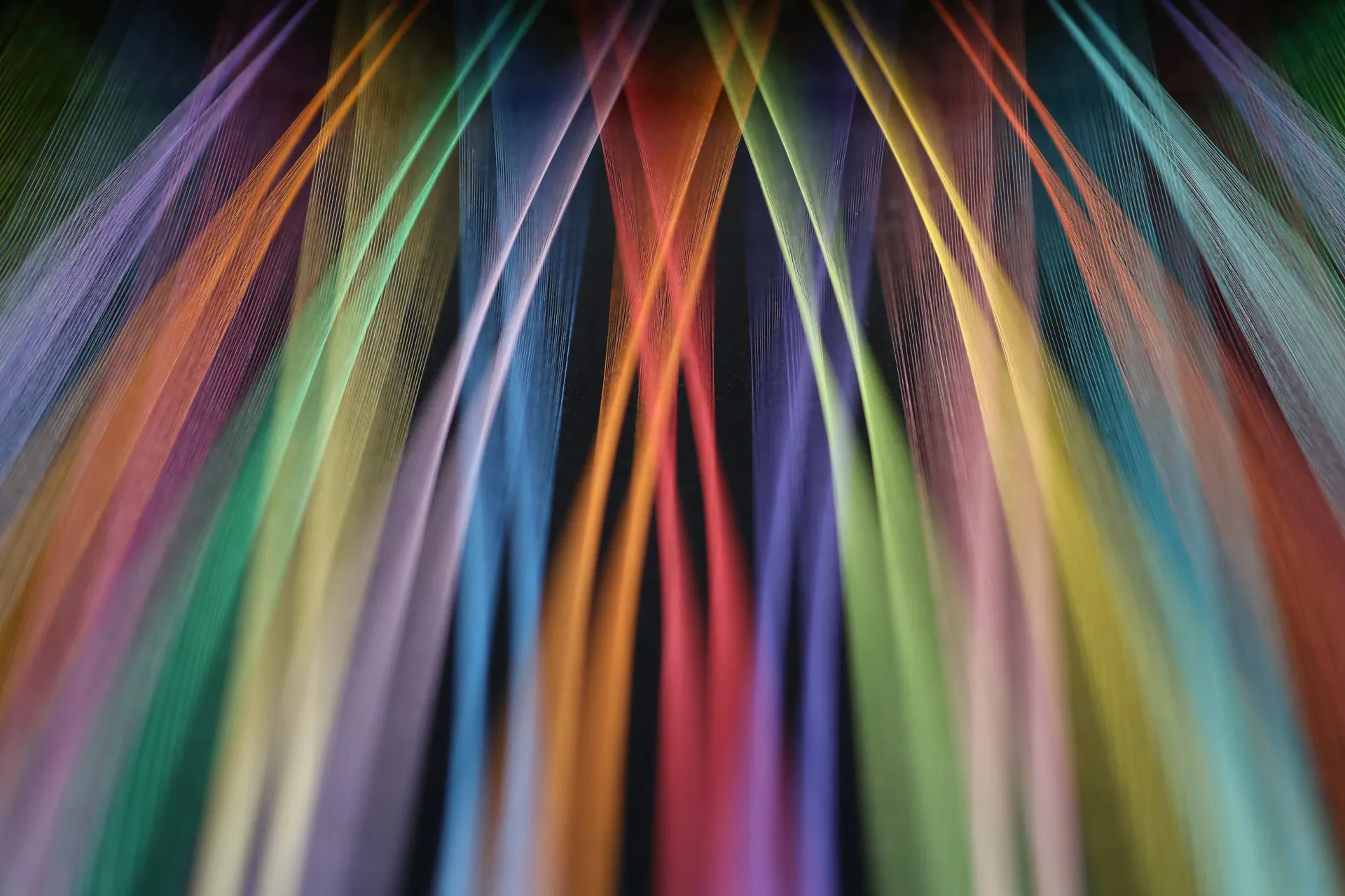 Colorful thread installation with rainbow strands converging dramatically against dark background
