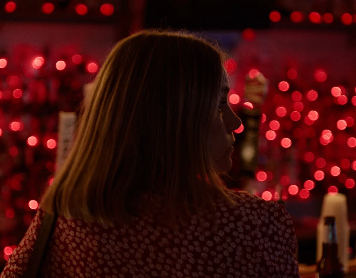 Silhouette of woman from behind surrounded by red bokeh lights in a bar setting