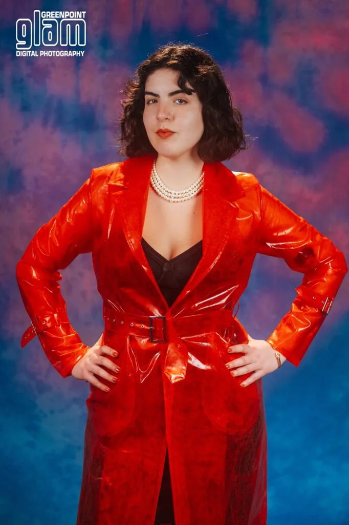 Woman in red patent leather coat with pearl necklace against colorful backdrop