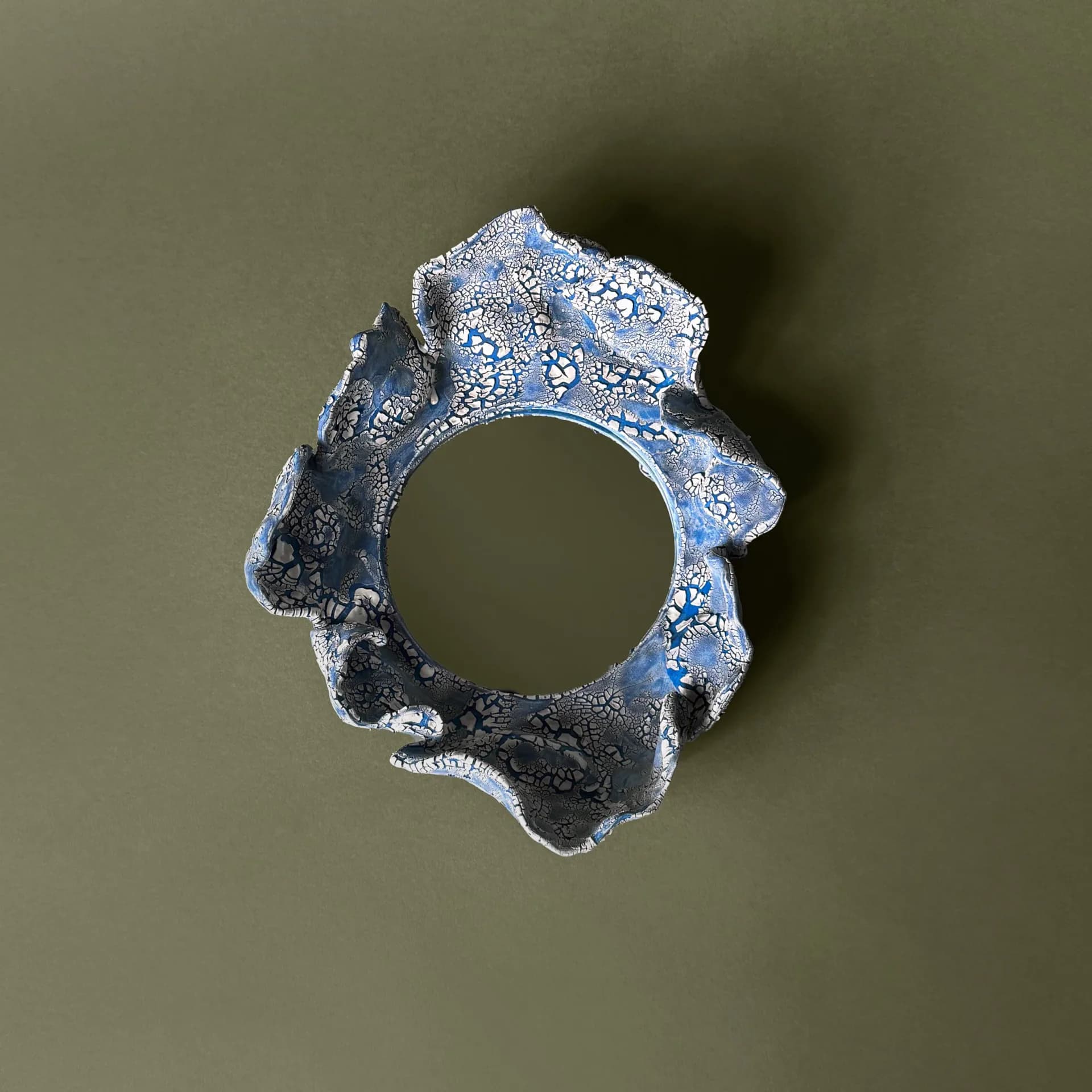 Blue and white crackle-glazed ceramic ring sculpture, overhead view on olive background