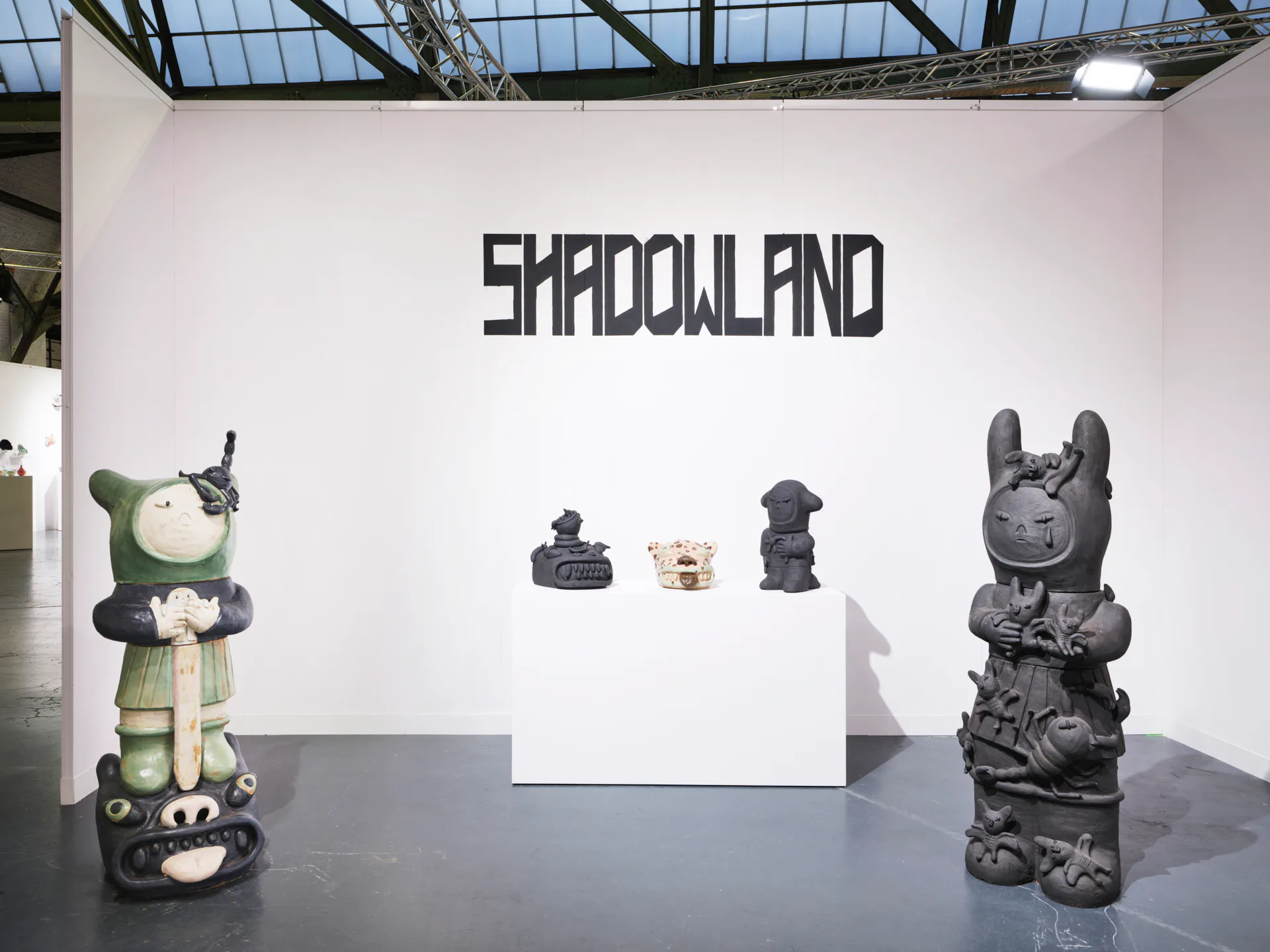 Large-scale ceramic sculpture installation with figurative totem-like forms and wall paintings of dark canine creatures