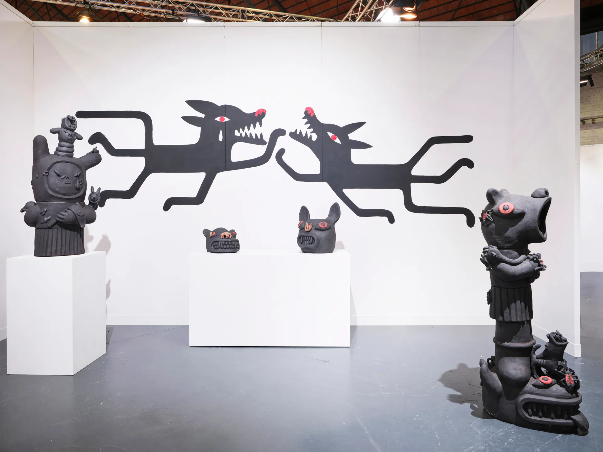 Installation view of ceramic sculptures and dark creature wall paintings in gallery booth